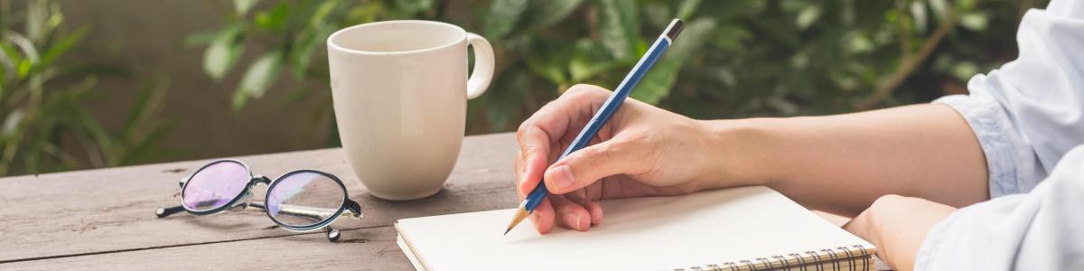 Person sidder ved et bord med papirblok, blyant og en kop kaffe